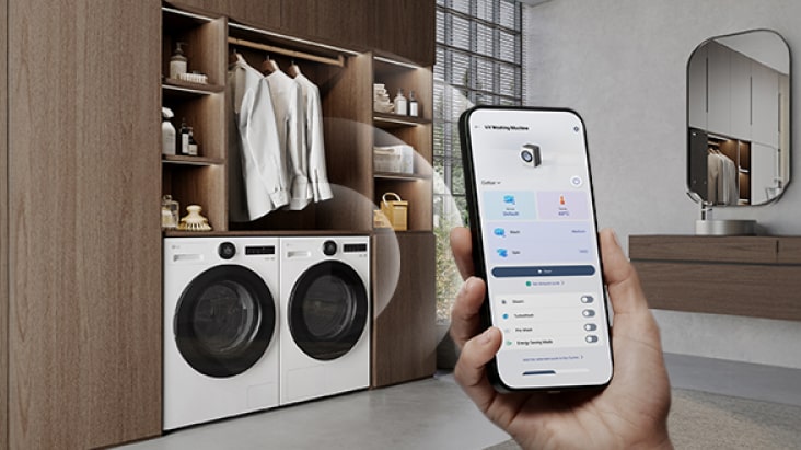 Lavadora-secadora LG en la parte inferior de un guardarropa con ropa y accesorios. Mano con smartphone con la app LG ThinQ.